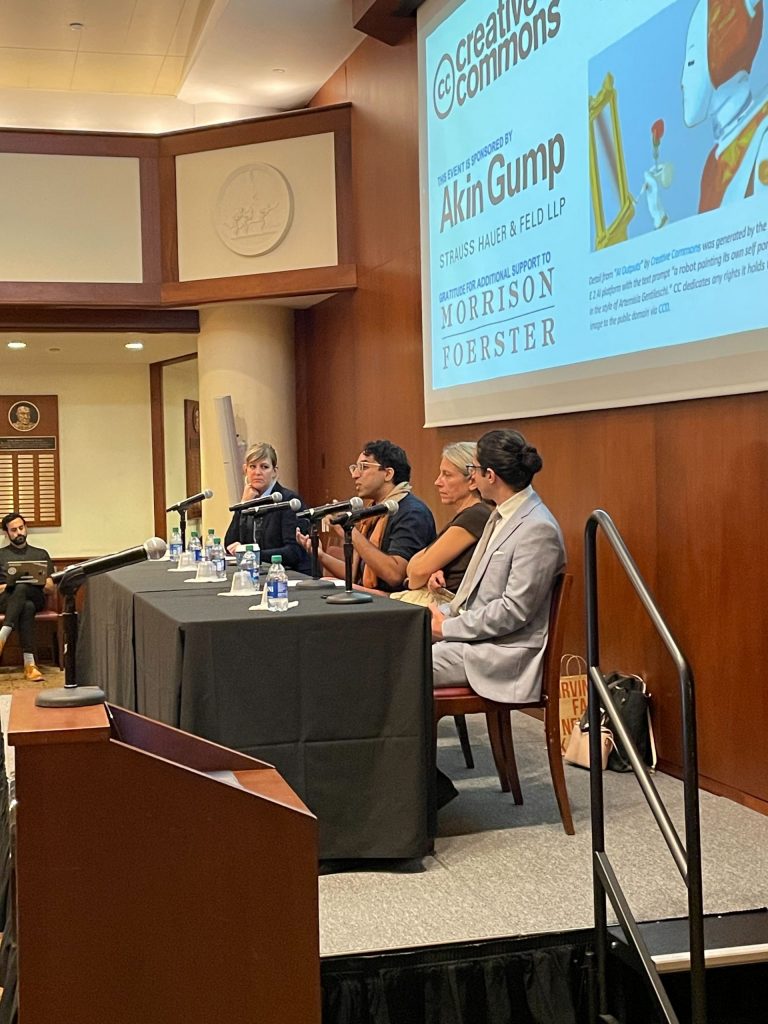 A panel of four people seated at a table on stage below a slide with an image of a robot painting at an empty easel, saying: Creative Commons, Engleberg Center on Innovation Law & Policy, this event sponsored by Akin, gratitude for additional support to Morrison Foerster.