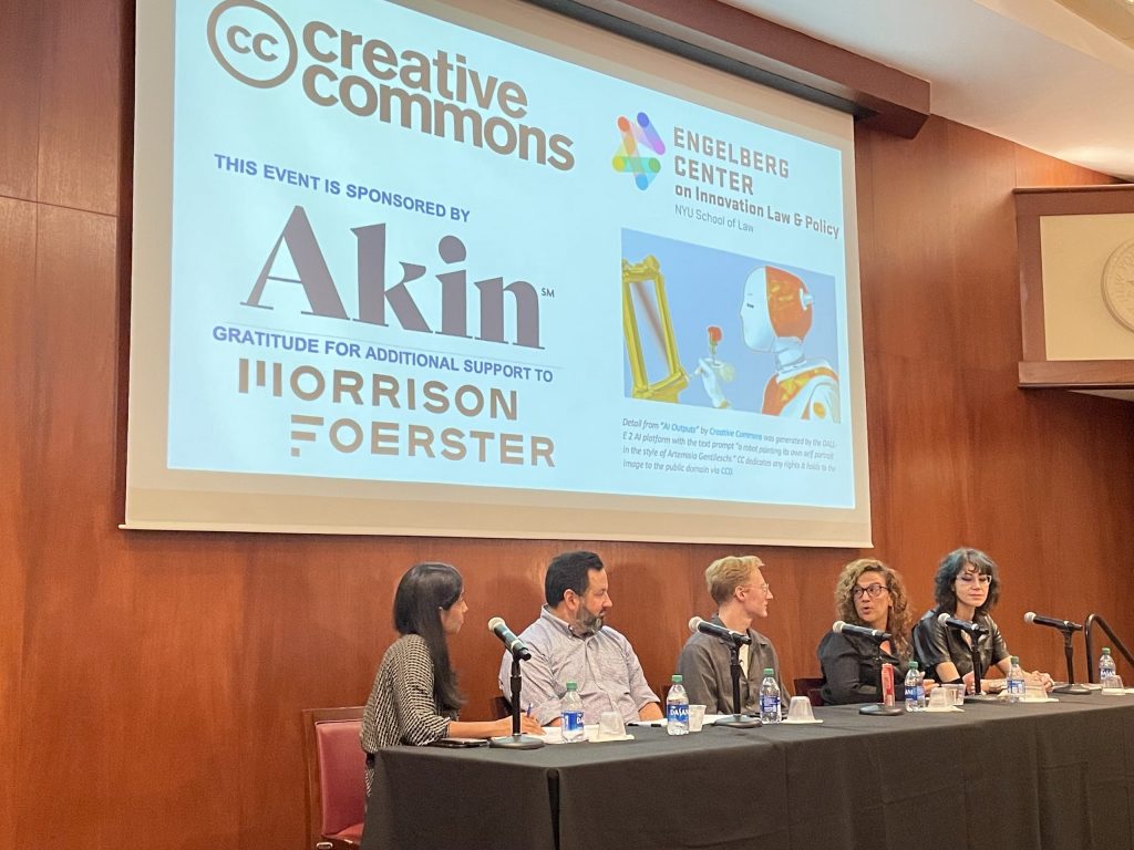 A panel of five people seated at a table on stage below a slide with an image of a robot painting at an empty easel, saying: Creative Commons, Engleberg Center on Innovation Law & Policy, this event sponsored by Akin, gratitude for additional support to Morrison Foerster.