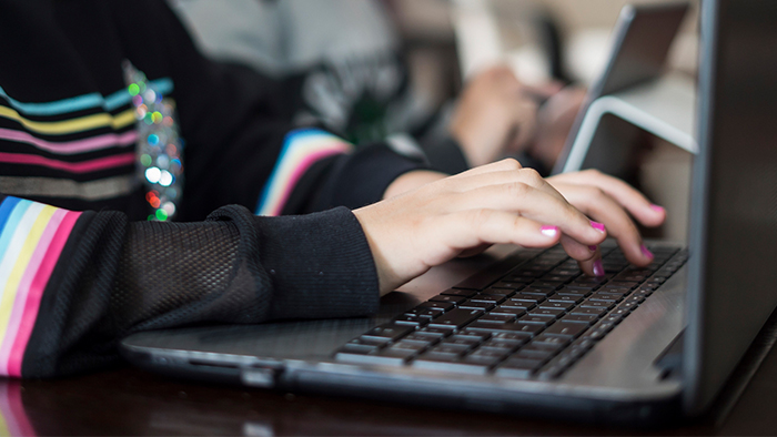 Hands with pink painted fingernails type on a laptop keyboard.